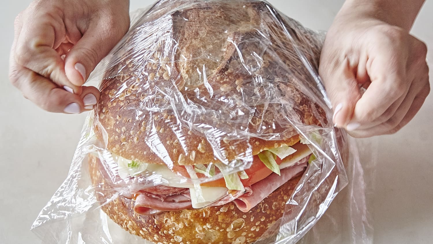 Sepasang tangan membungkus sandwich dengan plastic wrap bening